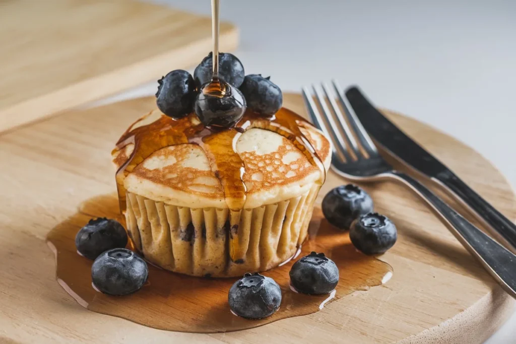 Plate of pancake muffins with various toppings like blueberries and chocolate chips, some muffins cut open to show their fluffy interior.